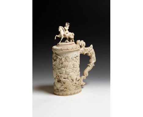 λ A fine and large late 19th century German carved ivory lidded tankard, probably Erbach, the finial carved with a warrior on