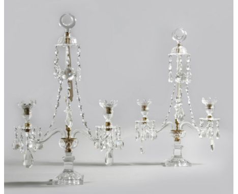 AMENDED A pair of George III style cut glass twin light candelabra, each with a crescent finial, above a triangular stem, wit