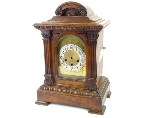 An early 20thC German walnut mantel clock, with arched engraved dial, silvered chaptering and carved case on block feet, (AF)