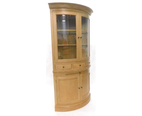 A light oak corner cabinet, the top with a moulded cornice, with two glazed doors enclosing glass shelves above three small d