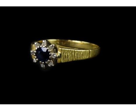 An 18ct gold sapphire and diamond cluster ring, with central round brilliant cut sapphire and tiny diamond border, on bark ef