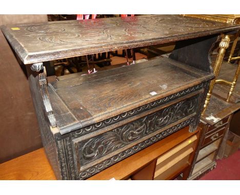 An early 20th century ebonised and floral relief carved oak fold-over monks bench, having typical hinged box seat base, width