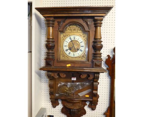 A circa 1900 Austrian carved walnut drop trunk wall clock, having arched enamel and gilt decorated dial, eight day movement w