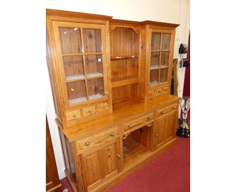 A contemporary pitched pine kitchen dresser, having twin glazed upper doors (one pane damaged), open two-tier central plate r