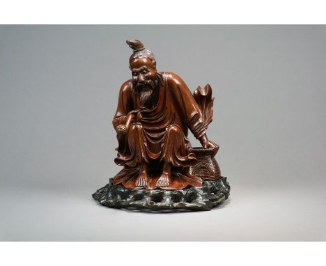 A Chinese carved root wood figure of a sage Late Qing Dynasty Modelled seated beside a basket, he wears flowing robes and hol