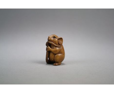 A Japanese carved wood netsuke of a rat Meiji/Taisho period Modelled seated on its hind legs, holding its long tail between i