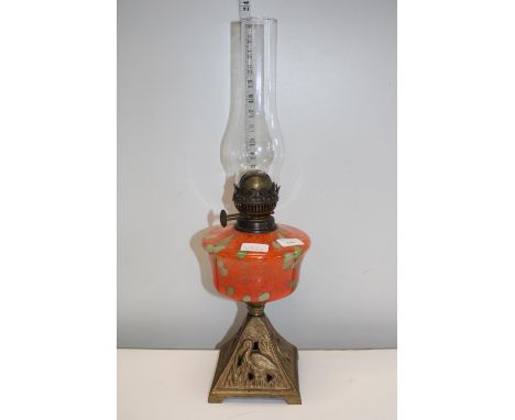 A brass and glass oil lamp with orange and green reservoir 