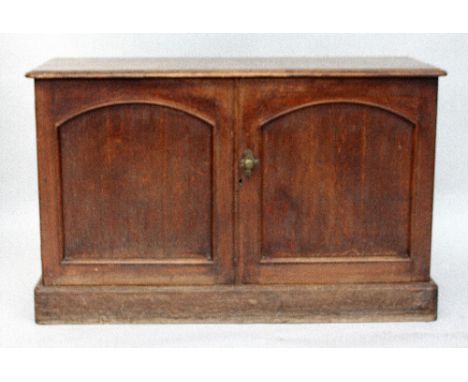 A Victorian oak cupboard, rectangular top with moulded edge, over two arched panel doors enclosing a shelf, with a platform b