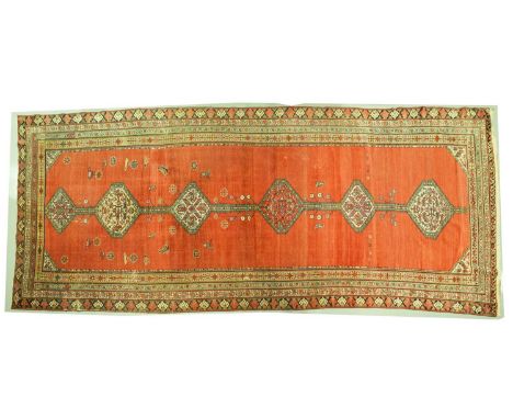 An antique tomato red ground North Western Persian long rug with six lozenges on a central pole within multiple borders. 466 