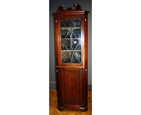 A late 19th century mahogany floor standing corner cupboard, the scrolled pediment over shaped barred glazed door enclosing f