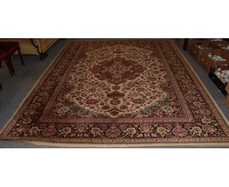 A machine made carpet of Oriental design, cream field with central medallion enclosed by floral borders, 338cm by 252cm