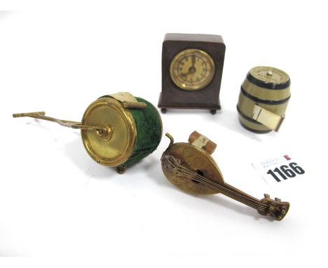 A Collection of Four Novelty Tape Measures, to include a bakelite clock, a lute, a barrel and a lawn roller, 4cm -10cm high. 