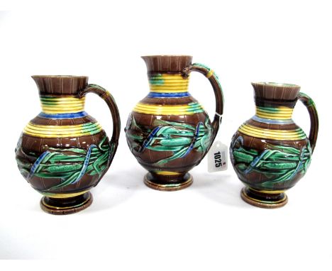 A Wedgwood Majolica Graduated Set of Three Pitcher Jugs, each of ovoid form with tapered necks, moulded and painted with bulr