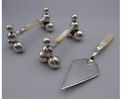 A pair of EPNS and mother-of-pearl knife rests and a mother-of-pearl and EPNS trowel. The latter 15.5 cm long.