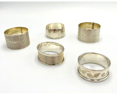 Two engine turned silver napkin rings together with three other silver napkin rings, 136g. Estimate: £70-100