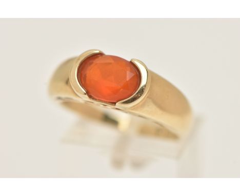 A 9CT GOLD GEM SET RING, an oval cut faceted orange stone, assessed as fire opal, half bezel set in yellow gold, leading on t