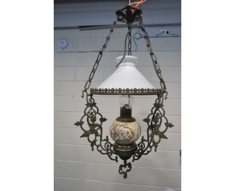 A 19TH CENTURY HANGING BRASS OIL LAMP, converted to electric, the flamboyant frame cradling a white glass shade, a bulbous ce