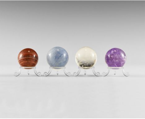 A group of four select, medium gemstone spheres, comprising one each of rock crystal, amethyst, blue calcite, and banded arag