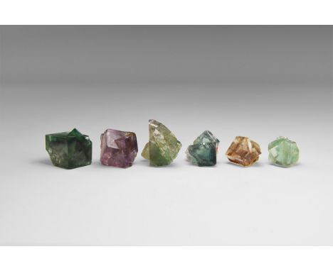 A group of five purple and one green fluorite crystals from Cumbria, most transparent and most twinned, in old white card tra