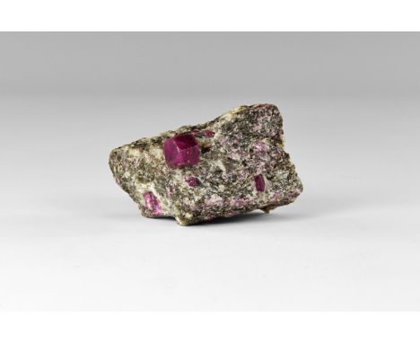 A classic, barrel-shaped ruby crystal on matrix, with several other matrix-bound ruby crystals, from India, in old white card