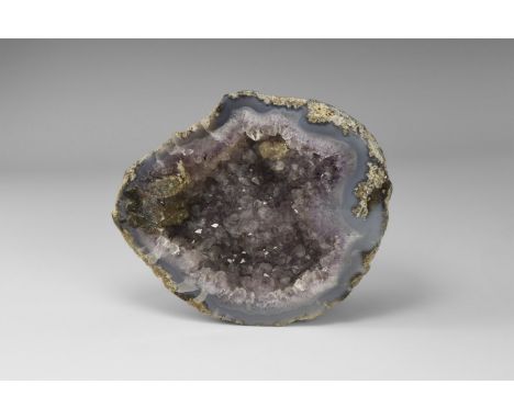 An agate geode filled with light lilac amethyst crystals with accessory brown calcite, from Brazil, in old white card tray. F