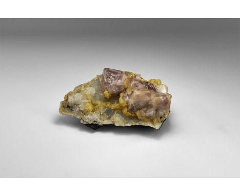 A specimen consisting of two large cubes of lavender fluorite with lustrous faces, accompanied by several smaller cubes, the 
