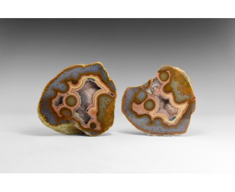 A sawn and polished pair of natural agate geodes with several 'eyes' and cavities filled with amethyst crystals, with stands.
