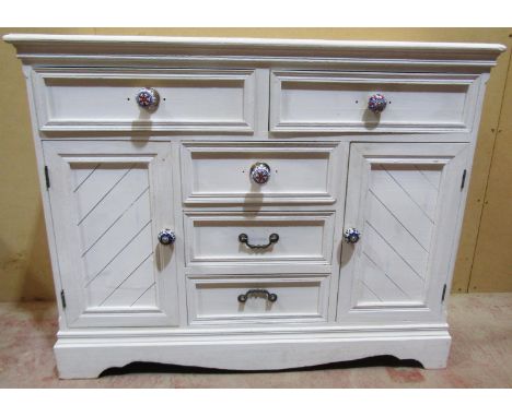 A over-painted pine chest of drawers, the base with panelled cupboard doors, fitted partially with polychrome porcelain handl