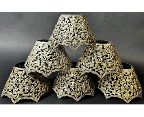 Six white metal pierced candlestick light shades with embossed and engraved Bacchanalian scenes of merriment, each with a sli