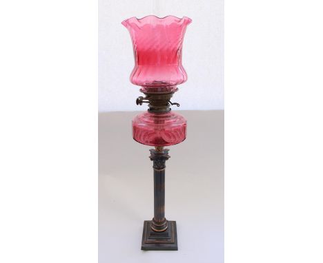 Early C20th oil lamp on burnished metal Corinthian column base with cranberry glass reservoir and matching shade and later fu