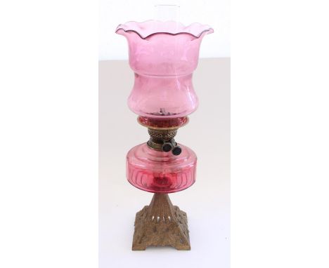 Early C20th oil lamp on moulded floral metal base with cranberry glass reservoir and etched cranberry glass shade and later f