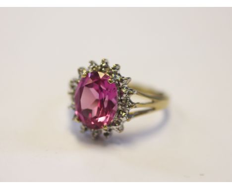 A pink sapphire and diamond set dress ring, the central oval sapphire within a white metal surround, bifurcated shoulders and