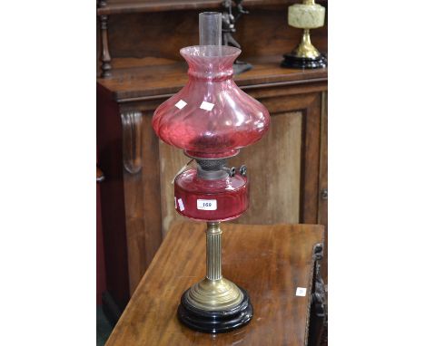 A Victorian cranberry glass oil lamp, brass corinthian column the twin burner with motif 