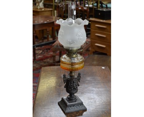 A Victorian cast iron oil lamp, twin handled urnular column cast with cherubs, supporting a faceted clear cut glass reservoir