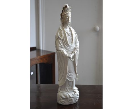 A Chinese blanc de chine figure, Guanyin, the deity standing, wearing flowing gowns, on a cloud scroll base, 48cm high, Qing
