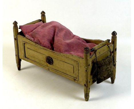 A late 19th century pine doll's bed, painted cream, with turned finials and decorative floral roundels, containing a hand sew