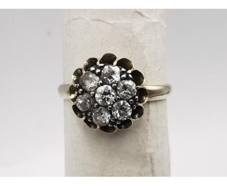 An early 20th century white metal (tests as 14 carat or higher) floral form diamond cluster ring. Set with seven round old cu