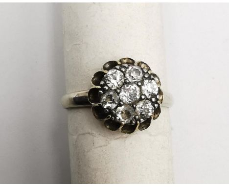 An early 20th century white metal (tests as 14 carat or higher) floral form diamond cluster ring. Set with seven round old cu
