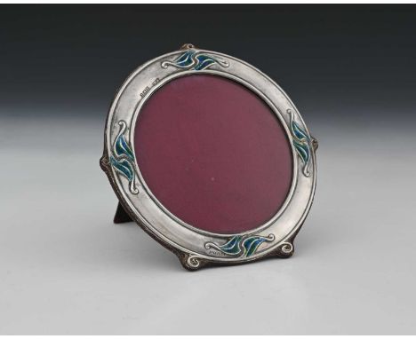 An Edwardian silver and enamel photograph frame, of circular form, the border adorned with foliate tendrils decorated in poly