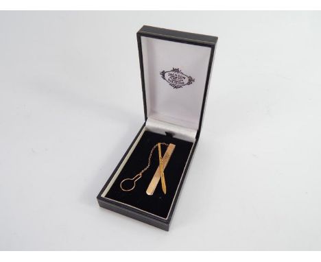 A 9ct gold tie slide modelled with a ski, with chain and button loop attachment, 10.5g.