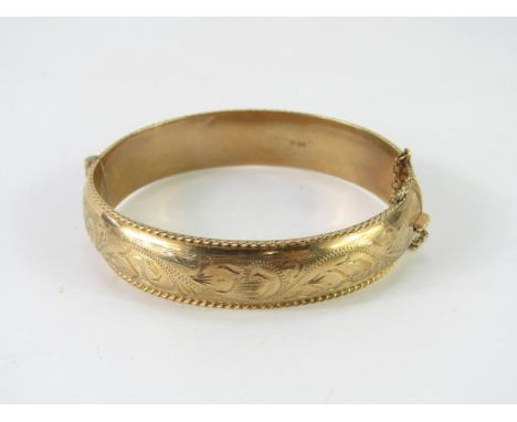 A 9ct gold bangle, with engraved foliate decoration, on a snap clasp with safety chain as fitted, 18.4g.
