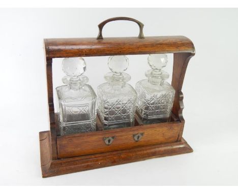 An early 20thC oak three bottle tantalus, containing two matching and one unmatched decanter, with brass carrying handle, 39c