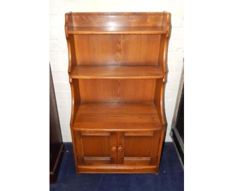 An Ercol light elm waterfall bookcase, with two shelves above two cupboard doors.