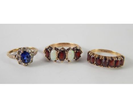 A 9ct gold and garnet seven stone ring, size M, garnet and opal five stone ring, stamped 9ct, size Q, and a 9ct gold tanzanit