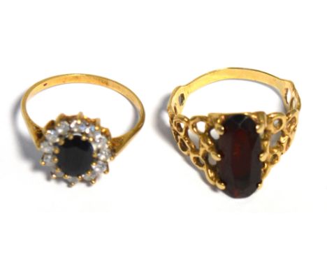 A yellow metal ring with scroll detail to the shoulders supporting a rectangular red stone, size R, and a yellow metal dress 