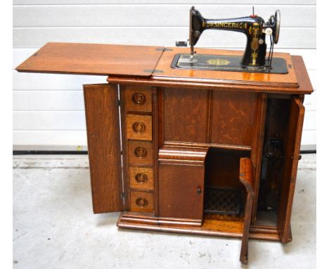 A 1920s/30s cabinet Singer treadle sewing machine with folding extension leaf, two bottom doors one side enclosing five small