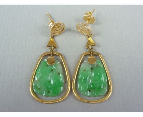 A pair of jade and yellow metal pendant earrings, with Chinese character ear stud, above a dependent carved jade drop, held p