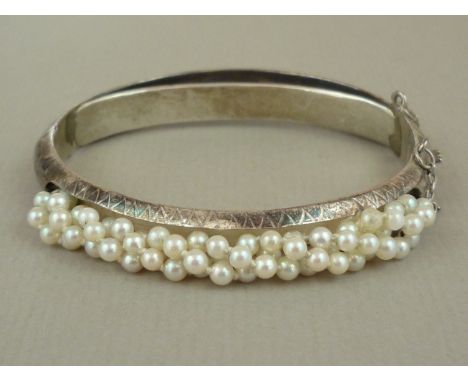 A seed pearl and silver hinged bangle, decoratively engraved and set to the face with threaded seed pearls, 18.9g