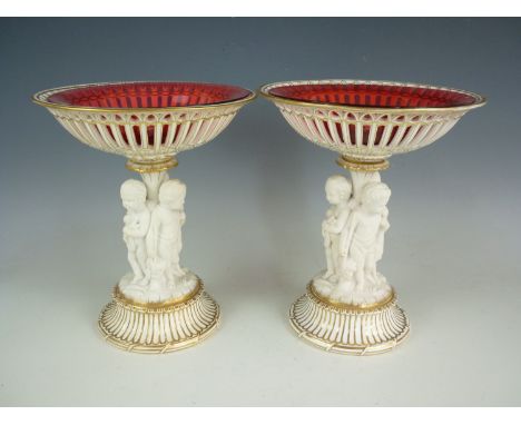 A pair of Victorian parcel glazed and gilded Parian table centrepieces, each having reticulated circular baskets, a figural s