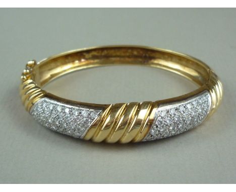 A diamond and high carat yellow metal hinged bangle, the face being spirally fluted surrounding two precious white metal and 